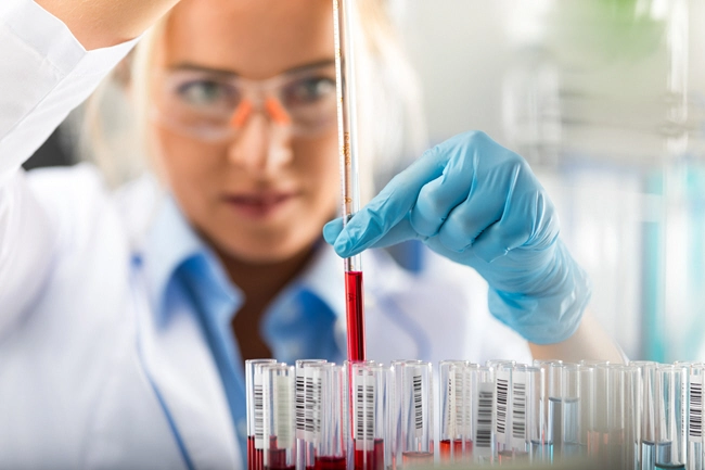 female scientist in protective eyeglasses and gloves dropping a red liquid substance into the test tube