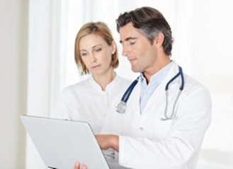 male doctor assisting his colleague while working on a laptop xs