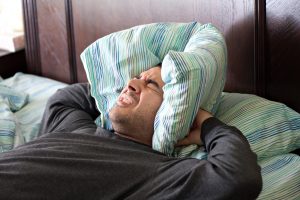 a man having trouble sleeping squeezes a pillow around his ears for some peace and quiet_Ht0bpVdASo 300x200