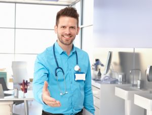 smiling doctor offering hand in exam room looking at camera 176818868 300x227